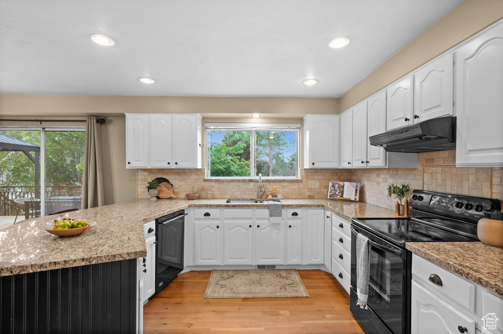 Kitchen with under cabinet range hood, black appliances, a sink, a peninsula, and plenty of natural light