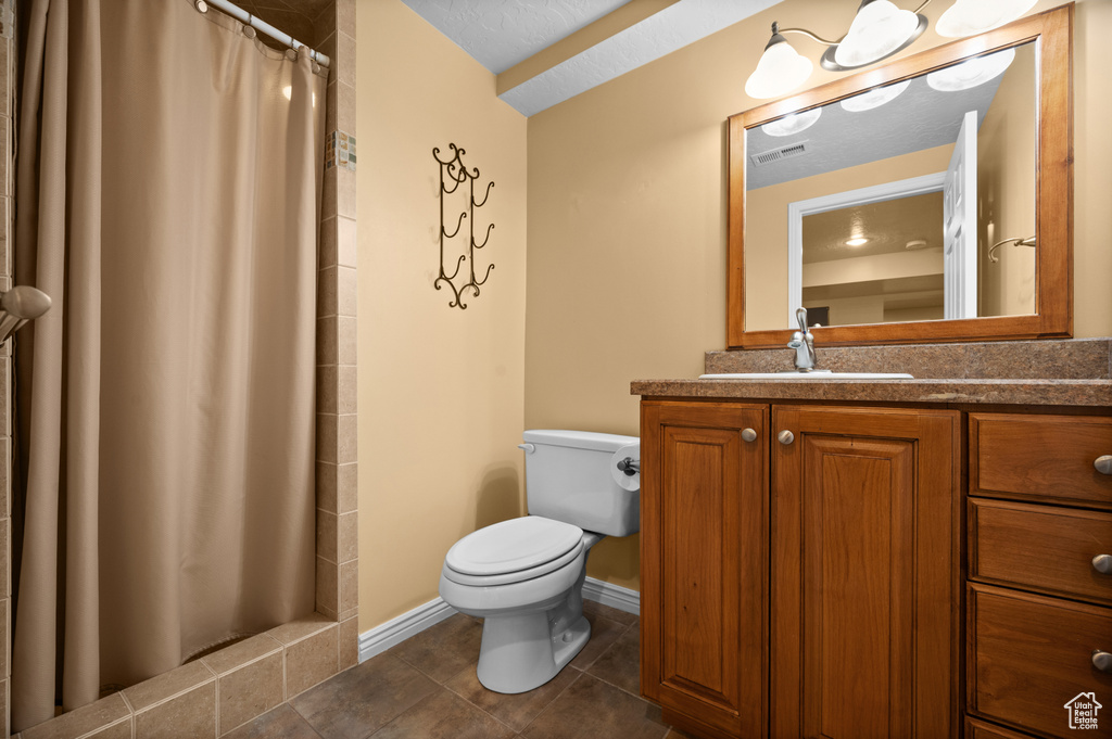 Full bathroom featuring toilet, tile patterned floors, vanity, tiled shower, and baseboards