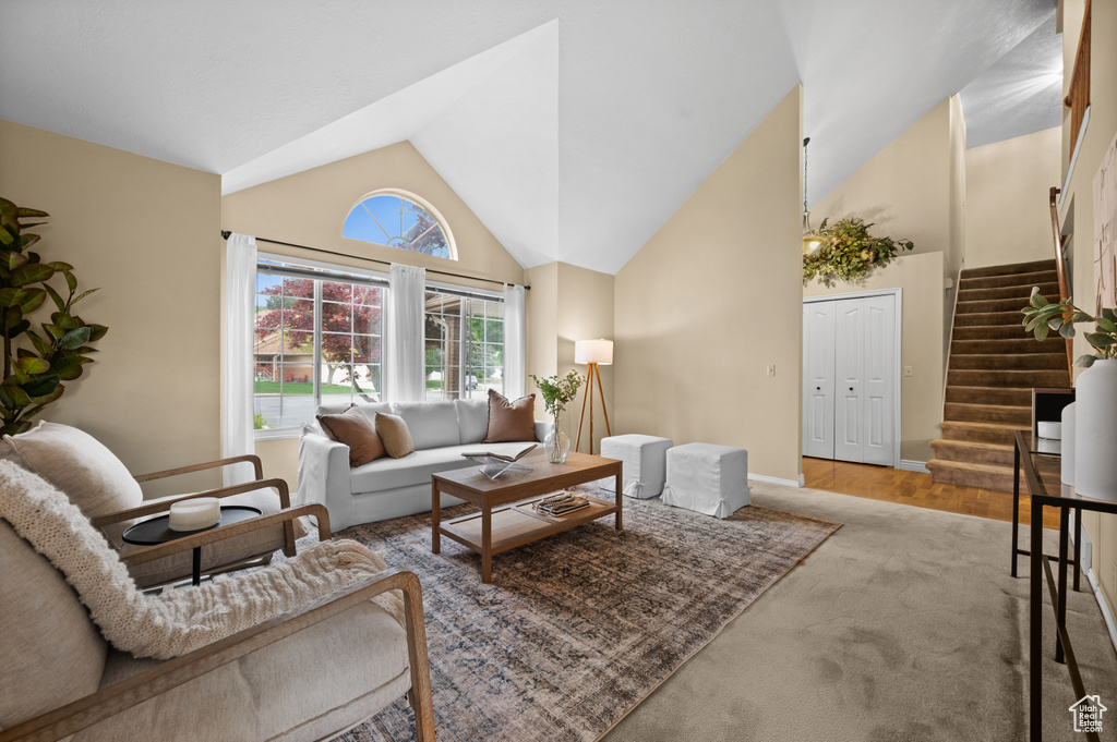 Carpeted living room with stairs, high vaulted ceiling, and baseboards