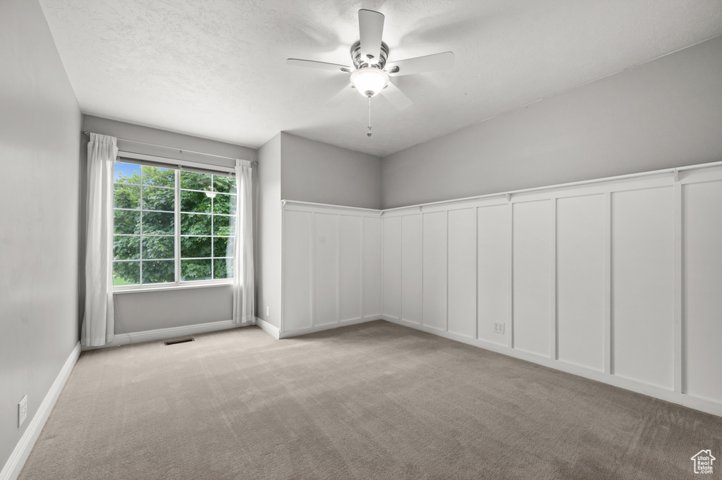 Carpeted spare room with ceiling fan, baseboards, and a decorative wall