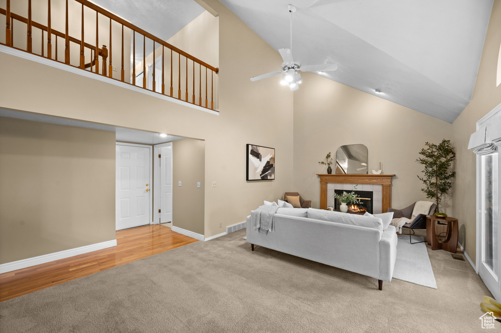Carpeted living area featuring a tile fireplace, high vaulted ceiling, baseboards, ceiling fan, and wood finished floors