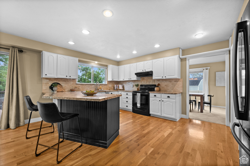 Kitchen featuring black appliances, a breakfast bar area, under cabinet range hood, white cabinetry, and light wood finished floors
