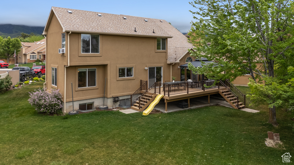 Rear view of house featuring stairs, a deck, a yard, stucco siding, and roof with shingles