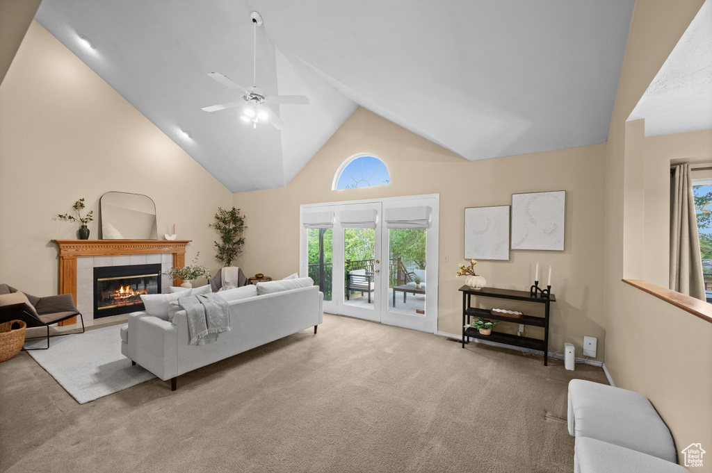 Carpeted living area featuring high vaulted ceiling, a tile fireplace, and a ceiling fan