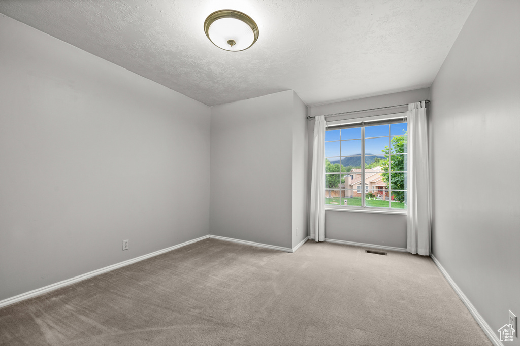 Spare room featuring a textured ceiling, carpet floors, and baseboards