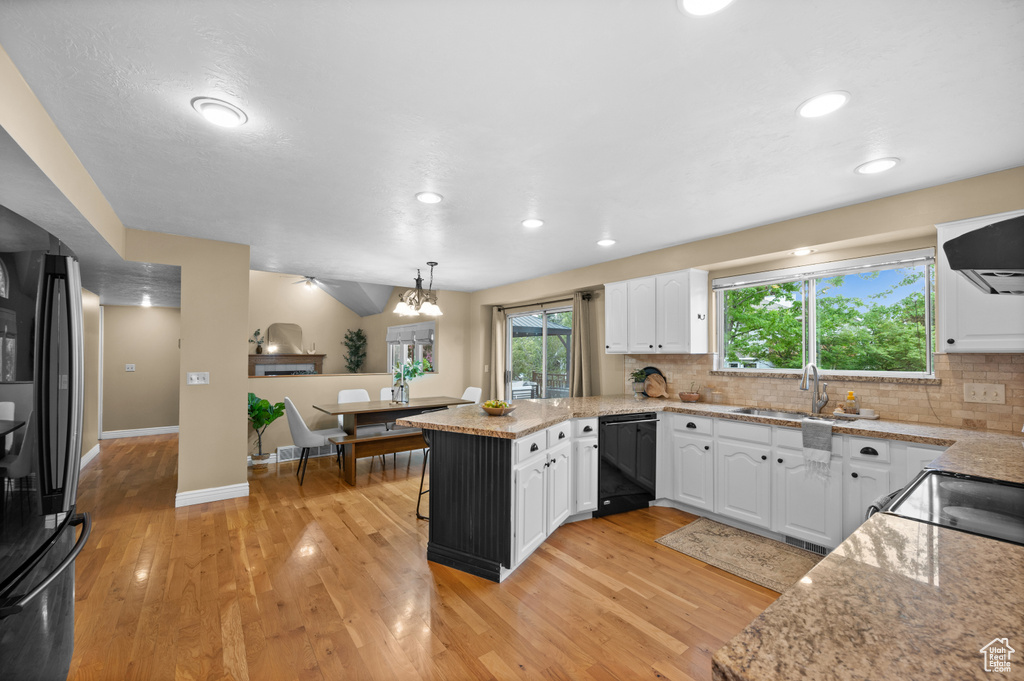 Kitchen featuring black appliances, a peninsula, a sink, white cabinetry, and light wood-style flooring