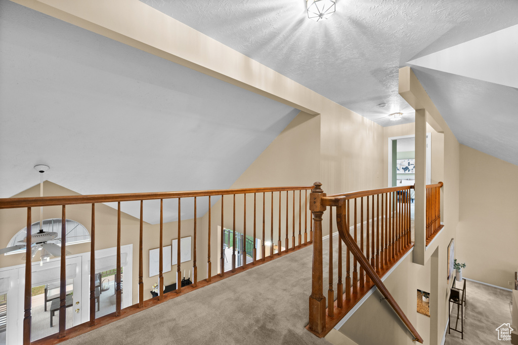 Hall with carpet, lofted ceiling, an upstairs landing, and a textured ceiling
