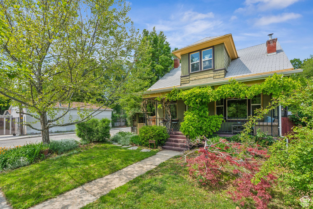 View of front of house with covered porch, a chimney, and a front yard