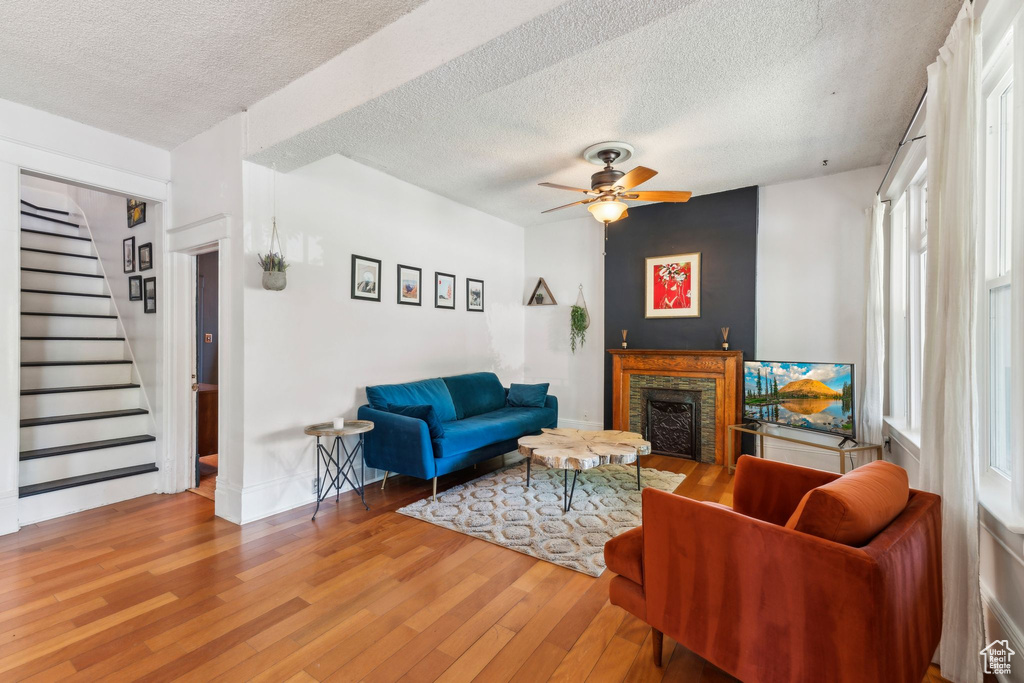 Living area featuring a textured ceiling, wood finished floors, a fireplace, stairway, and a ceiling fan
