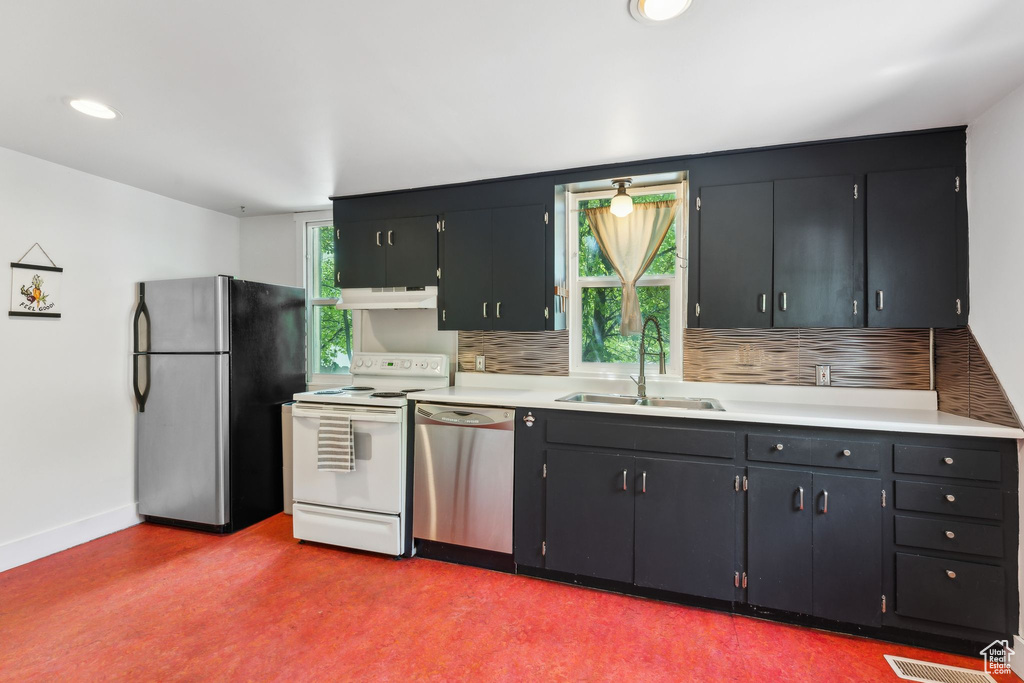 Kitchen with appliances with stainless steel finishes, under cabinet range hood, a sink, and decorative backsplash
