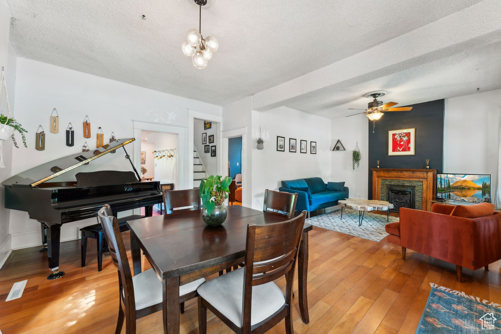 Dining room featuring stairway, light wood-type flooring, a fireplace, ceiling fan, and a textured ceiling