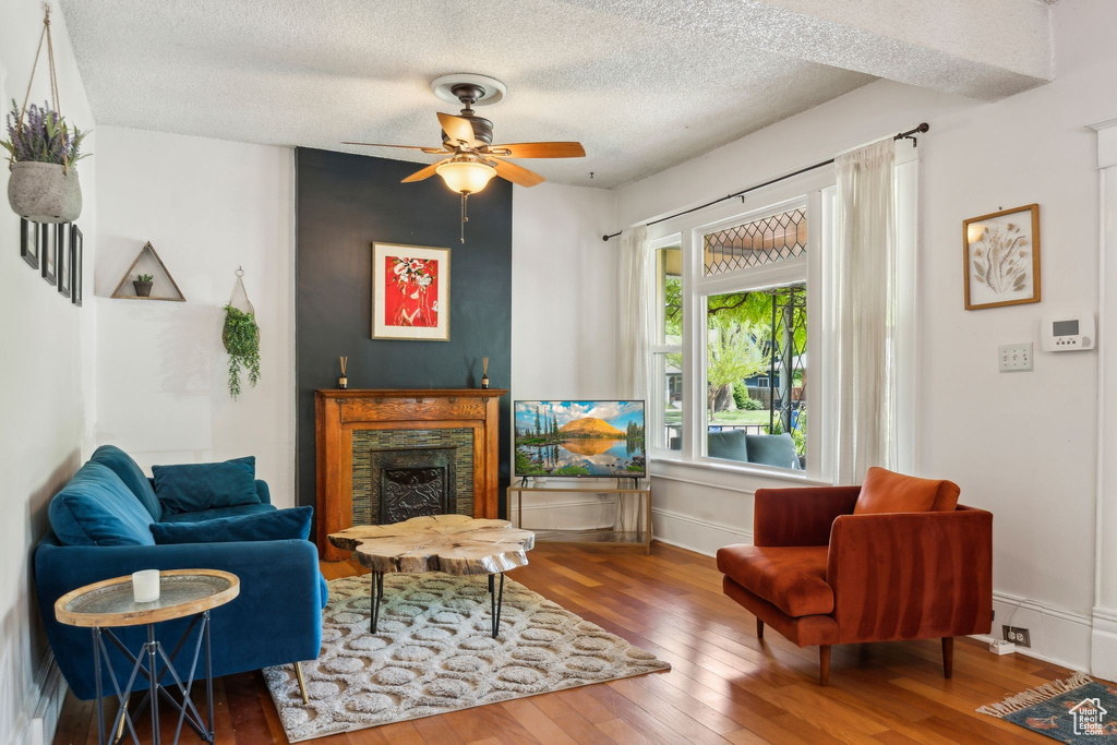 Living area with wood-type flooring, a fireplace, a textured ceiling, ceiling fan, and baseboards