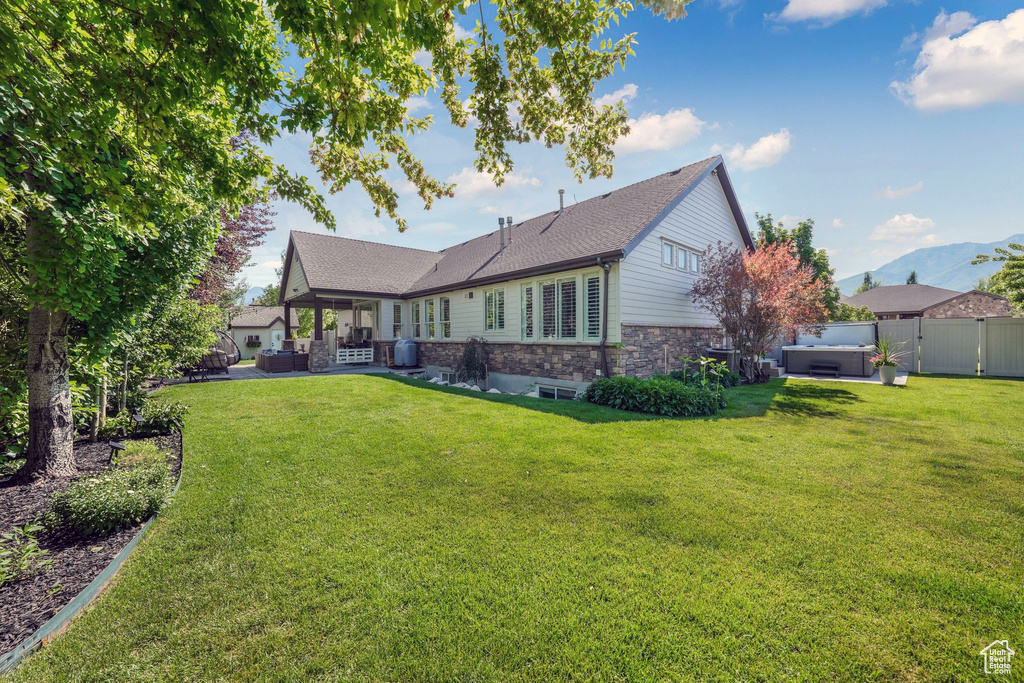 Rear view of house with a hot tub, stone siding, a patio, roof with shingles, and an outdoor living space