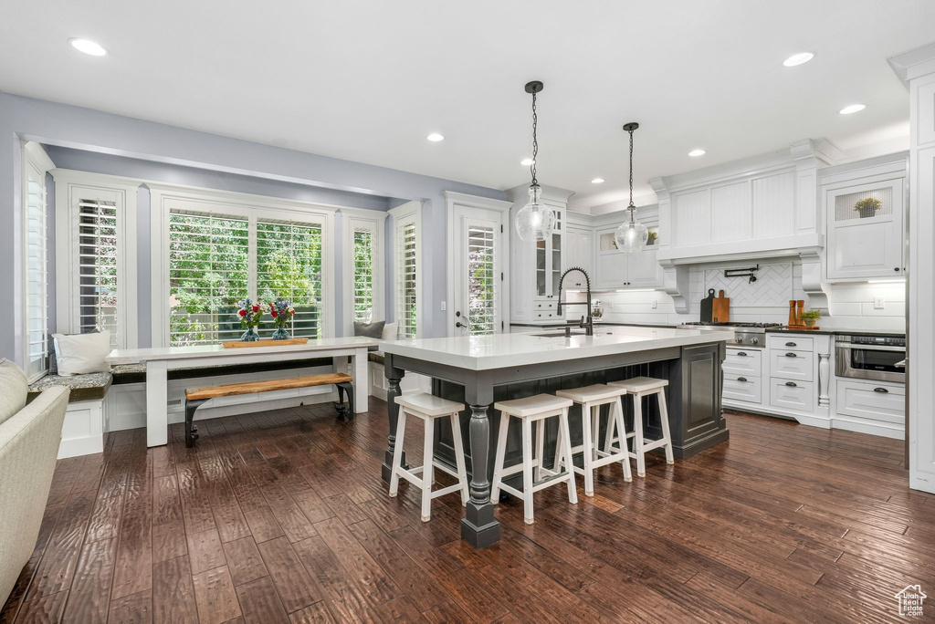 Kitchen with glass insert cabinets, tasteful backsplash, an island with sink, a kitchen bar, and dark wood-type flooring