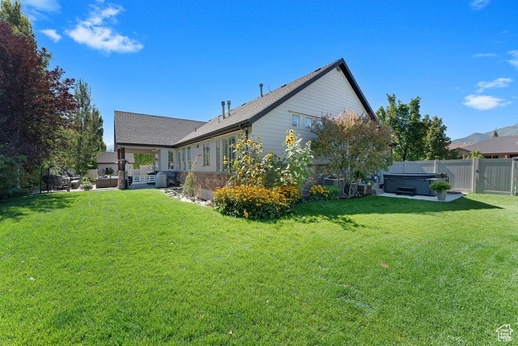 Back of house with a hot tub, a patio, and a shingled roof