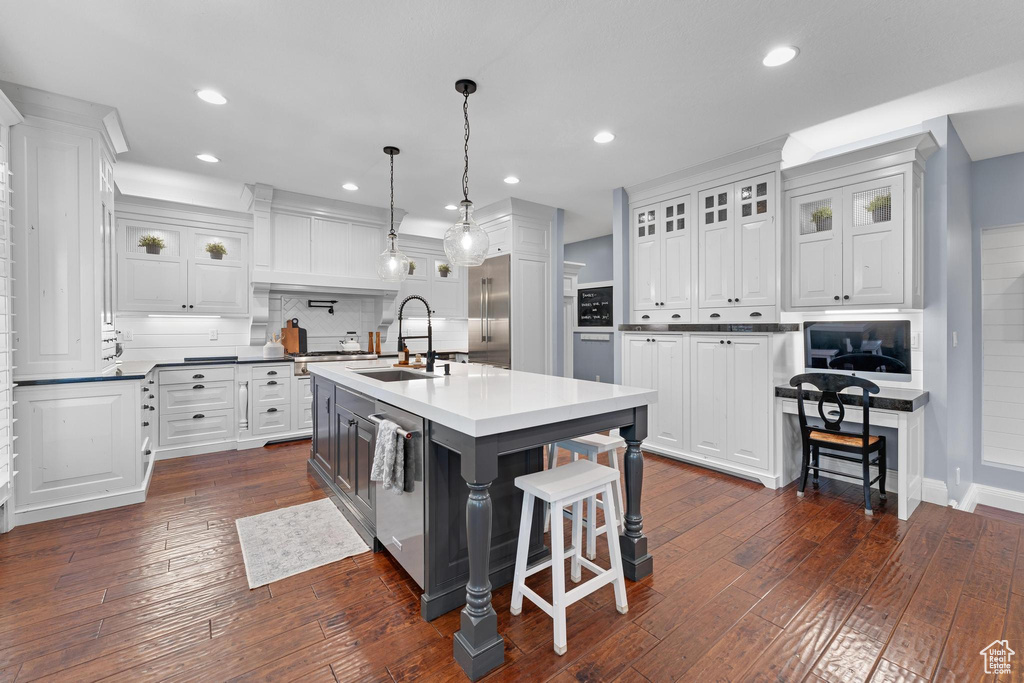Kitchen with a sink, an island with sink, white cabinets, a kitchen bar, and backsplash