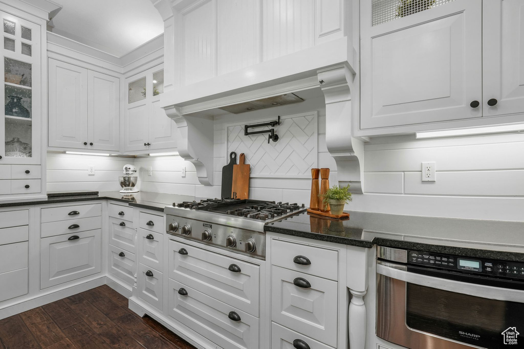 Kitchen with stainless steel appliances, white cabinets, tasteful backsplash, dark wood-style flooring, and glass insert cabinets
