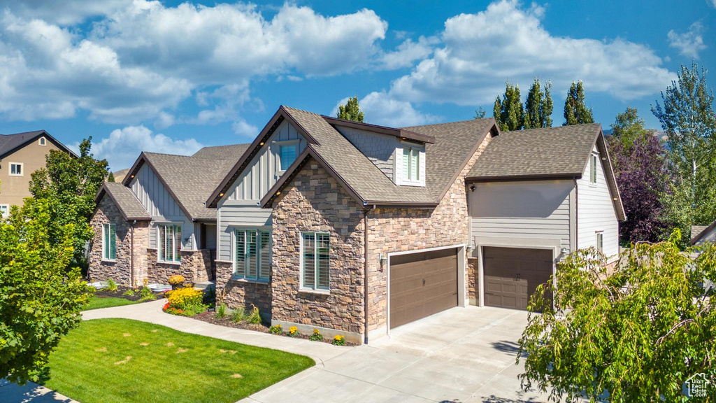 Craftsman-style home featuring board and batten siding, stone siding, driveway, a shingled roof, and a garage