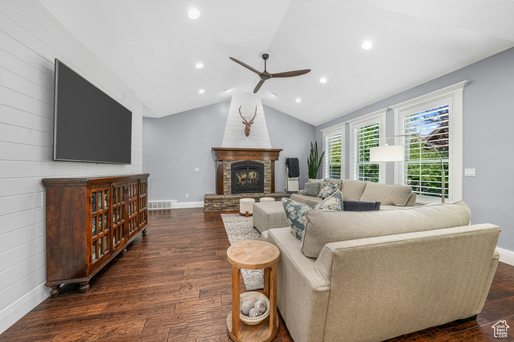 Living room with ceiling fan, a glass covered fireplace, dark wood-type flooring, recessed lighting, and lofted ceiling