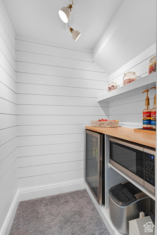 Laundry room featuring wine cooler, a bar, carpet flooring, baseboards, and wood walls