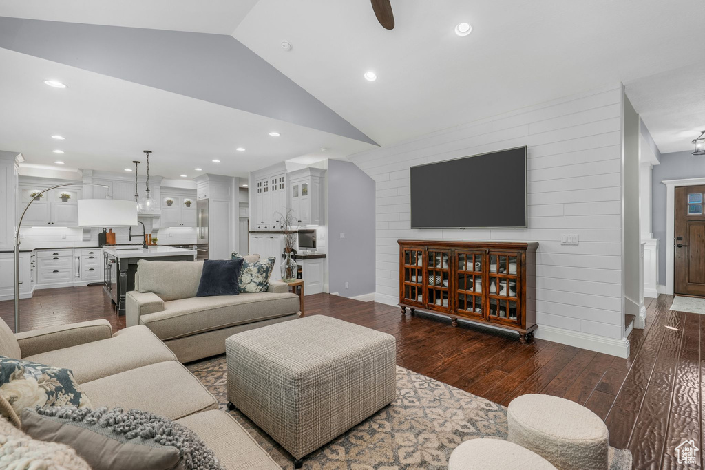 Living room featuring vaulted ceiling, dark wood finished floors, wood walls, recessed lighting, and a ceiling fan