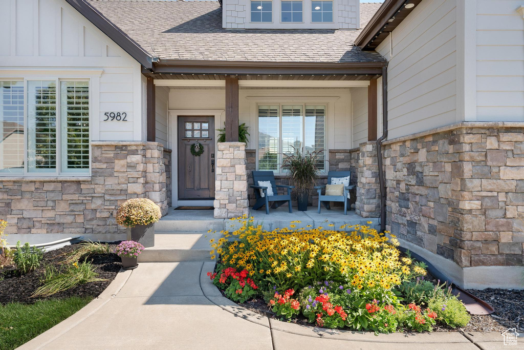 Entrance to property featuring a porch, stone siding, roof with shingles, and board and batten siding