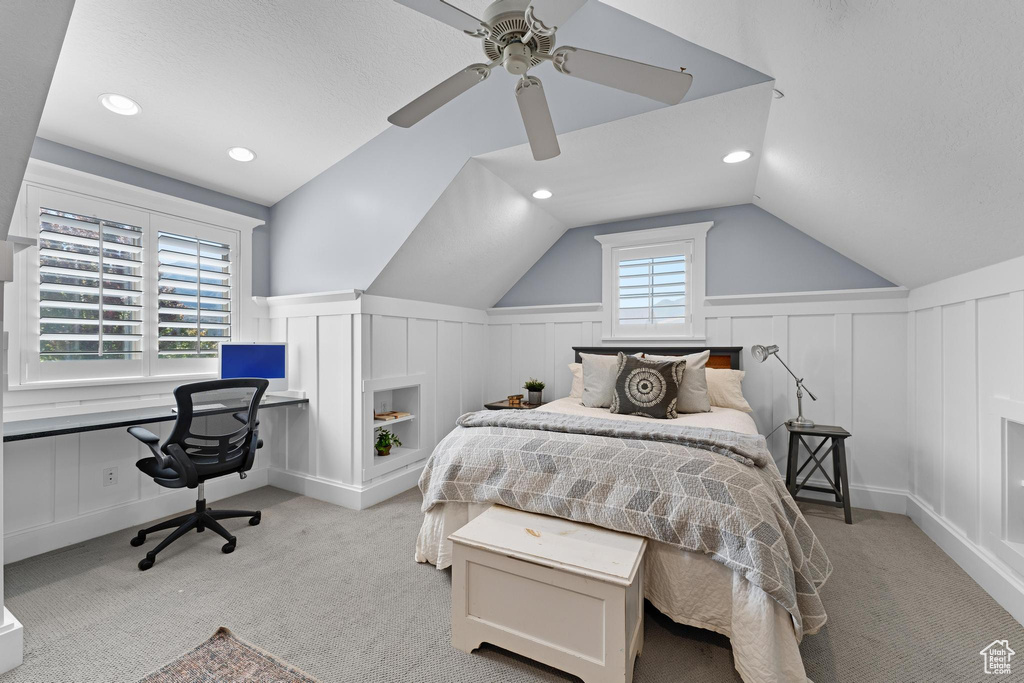 Bedroom featuring a decorative wall, light carpet, vaulted ceiling, a ceiling fan, and a wainscoted wall