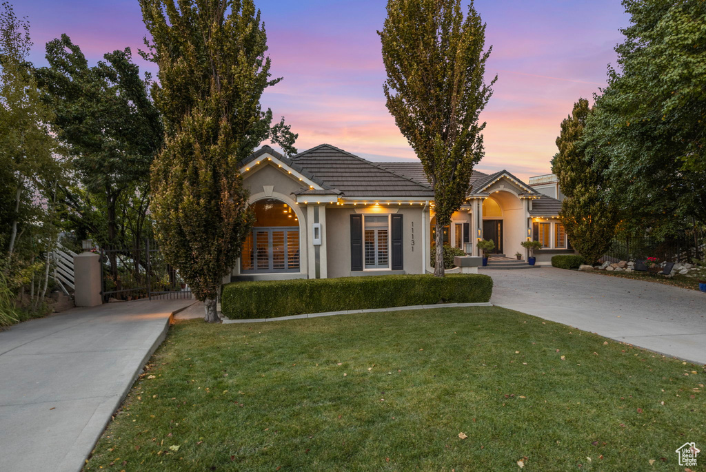 View of front facade with concrete driveway, a tiled roof, a lawn, and stucco siding