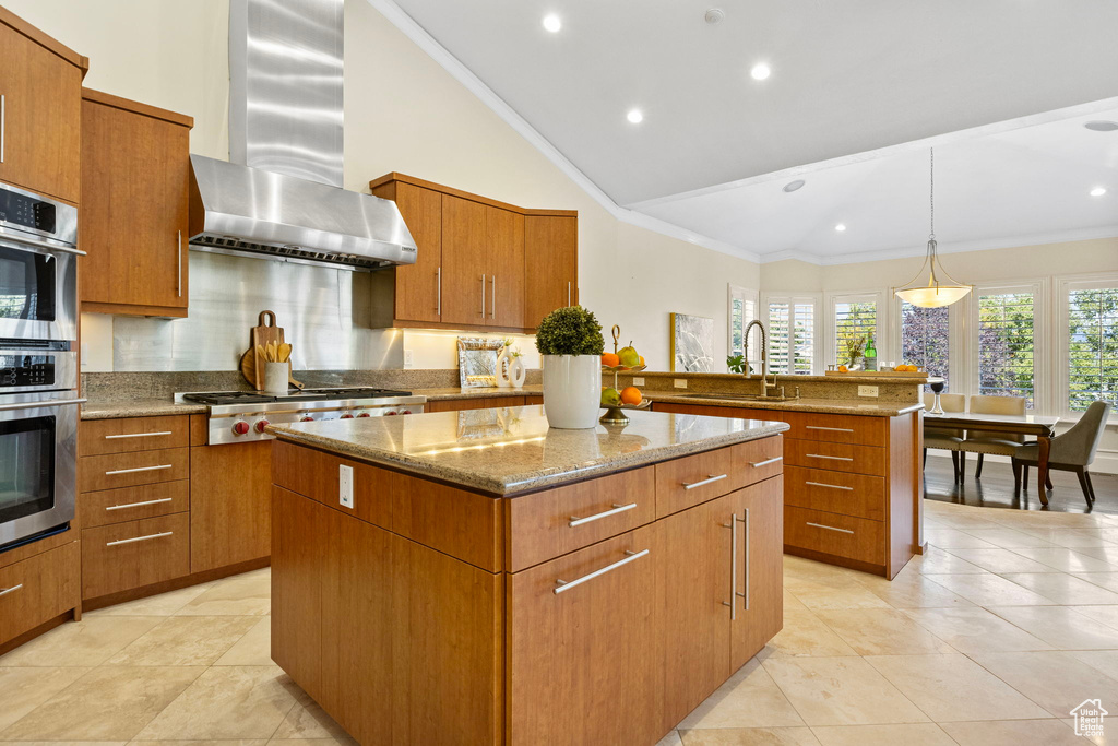 Kitchen with wall chimney range hood, a sink, a center island, stainless steel appliances, and light stone countertops