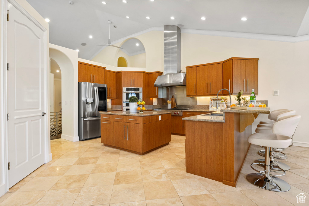 Kitchen featuring stainless steel appliances, wall chimney exhaust hood, a sink, brown cabinets, and high vaulted ceiling