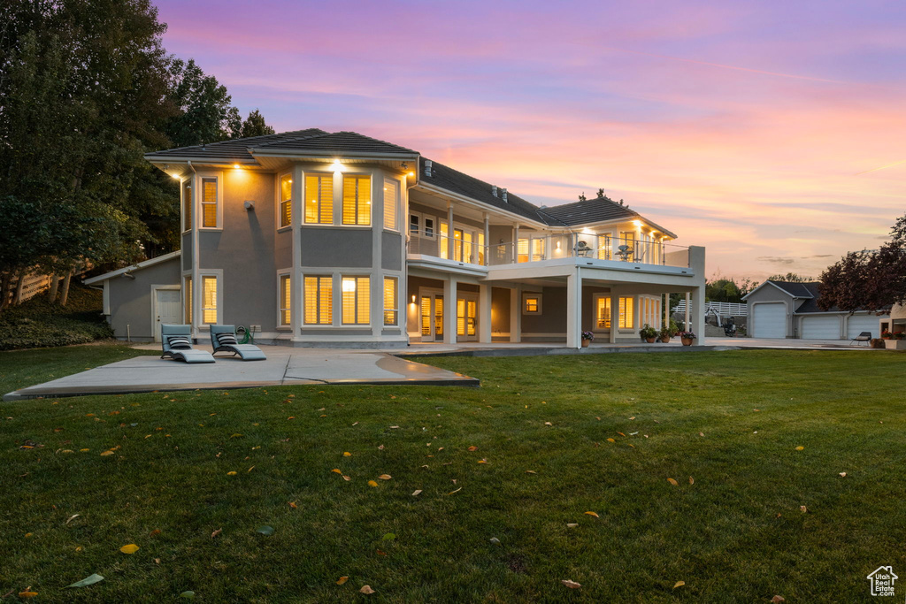 Rear view of house with a balcony, a lawn, a patio area, and stucco siding