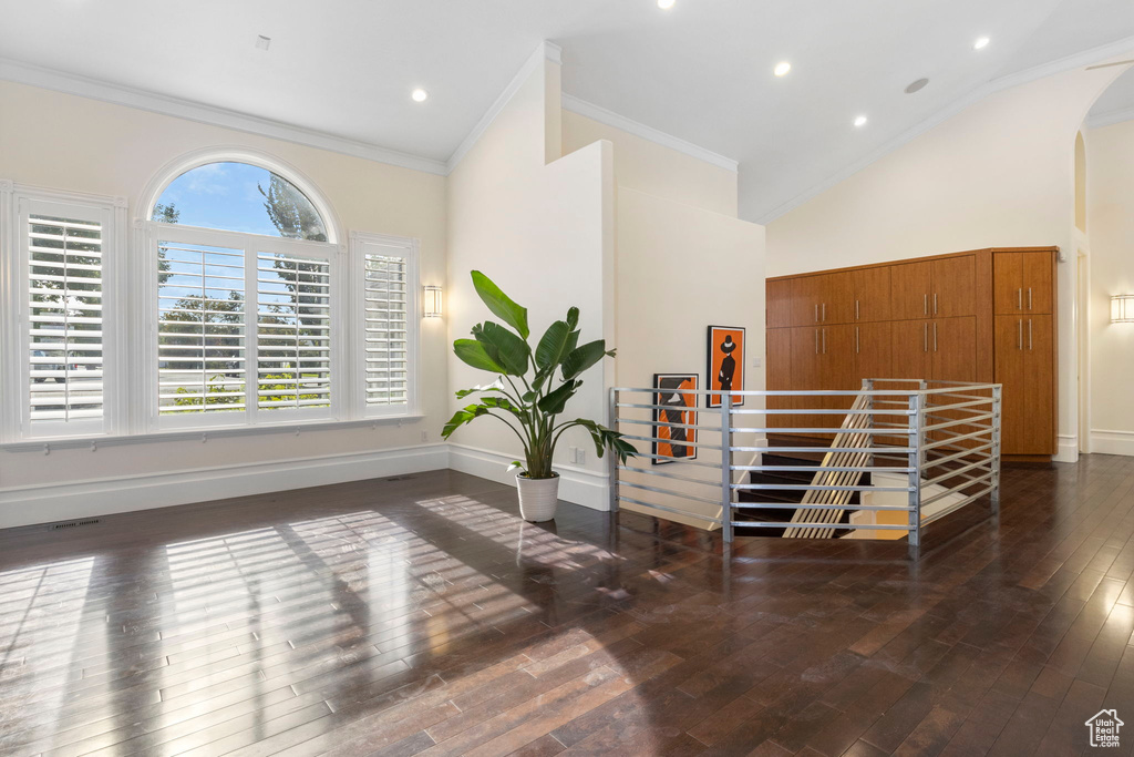 Interior space featuring arched walkways, hardwood / wood-style floors, high vaulted ceiling, baseboards, and ornamental molding