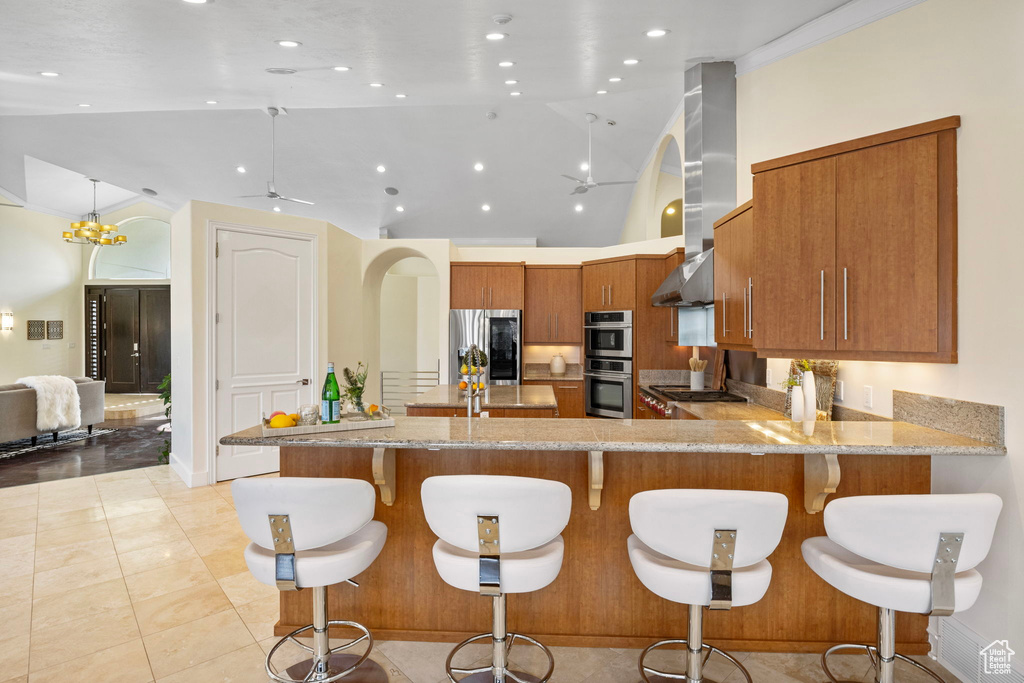 Kitchen with stainless steel appliances, a peninsula, brown cabinets, light stone countertops, and ceiling fan