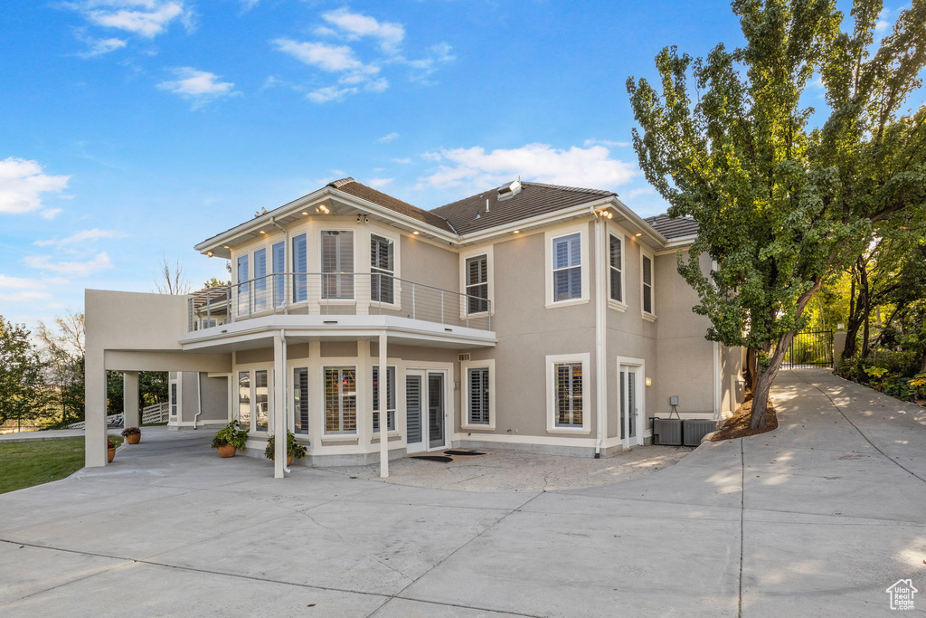 Back of property featuring a balcony, driveway, a carport, and stucco siding