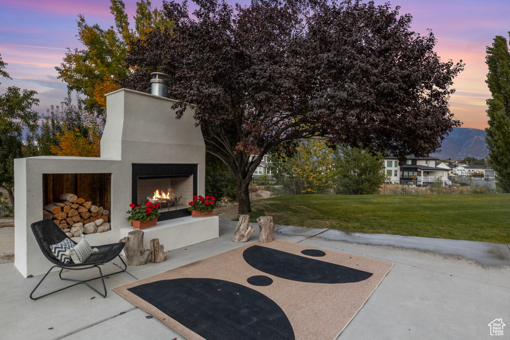 Patio terrace at dusk with a lit fireplace and a lawn