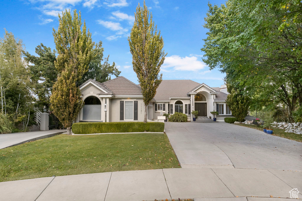 Ranch-style house with concrete driveway, a tiled roof, a front lawn, and stucco siding
