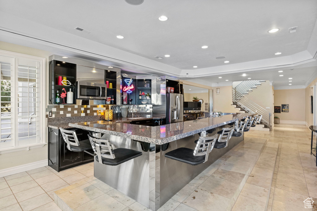 Indoor wet bar with a tray ceiling, recessed lighting, baseboards, appliances with stainless steel finishes, and stairway
