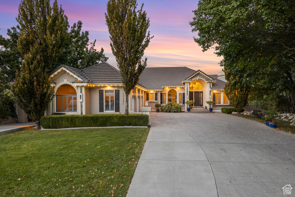 View of front of home featuring concrete driveway, a tile roof, a yard, and stucco siding