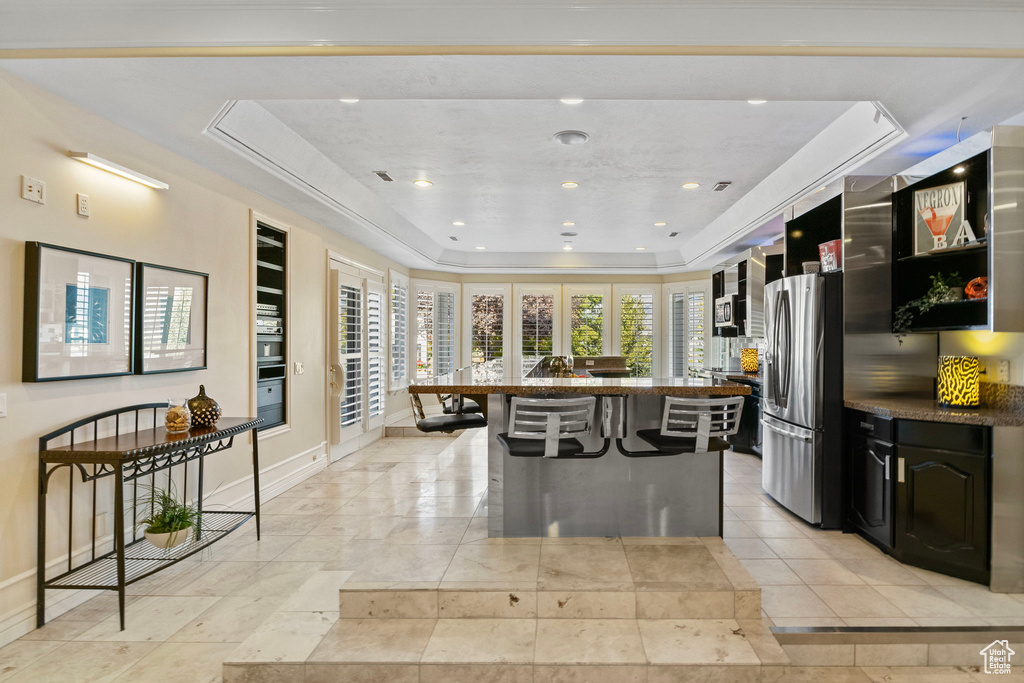 Kitchen featuring stainless steel fridge with ice dispenser, a tray ceiling, a kitchen bar, baseboards, and a kitchen island