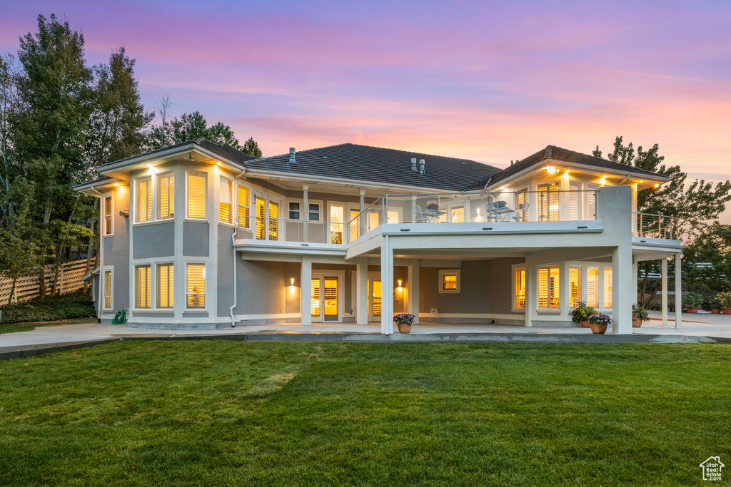 Back of house at dusk with a balcony, a patio area, and stucco siding