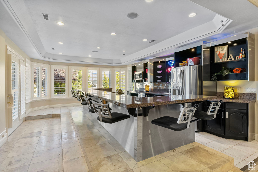 Bar area featuring a tray ceiling, stainless steel fridge, recessed lighting, light tile patterned floors, and a sink