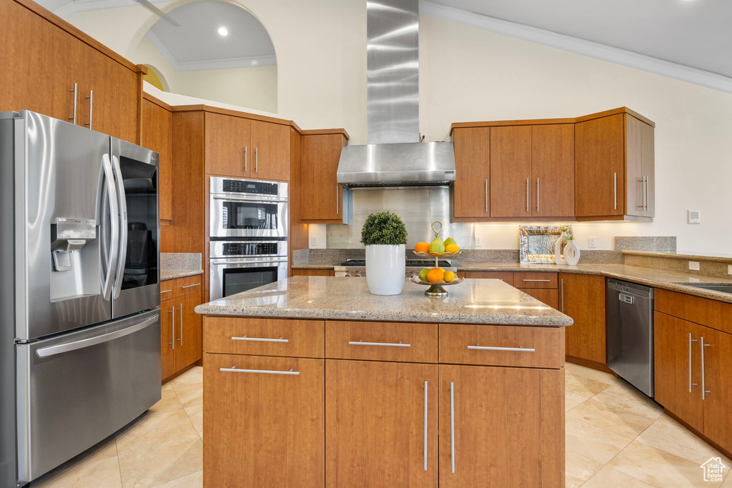 Kitchen with stainless steel appliances, wall chimney exhaust hood, a center island, light stone countertops, and ornamental molding