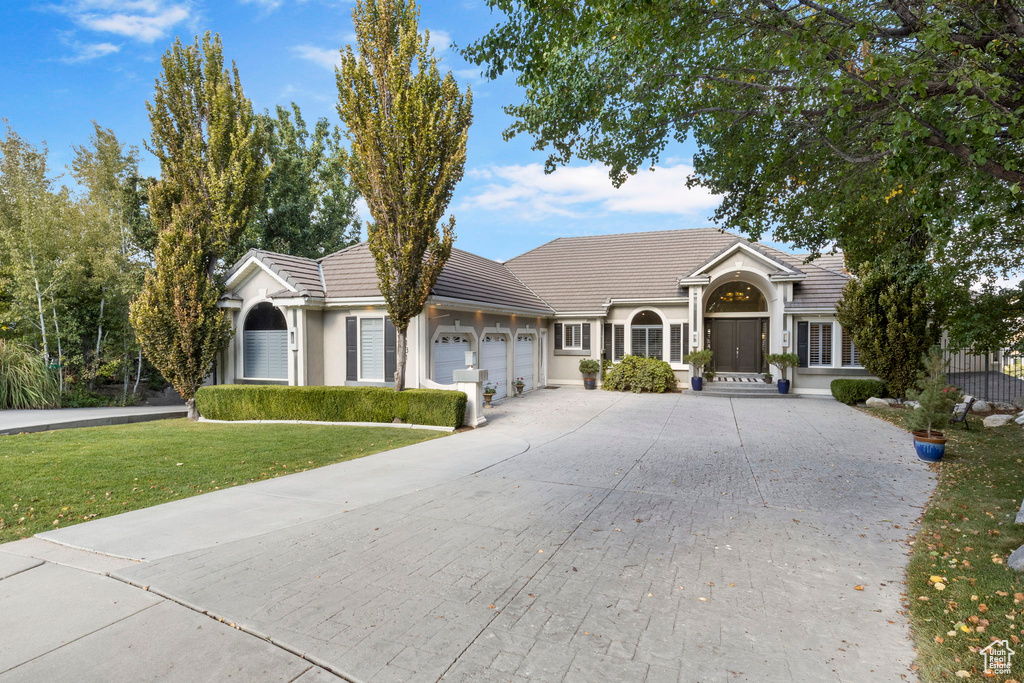 Single story home featuring a garage, a front lawn, driveway, a tile roof, and stucco siding