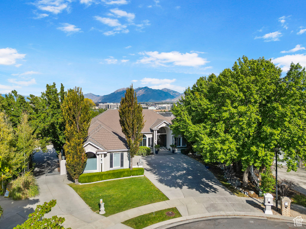 View of property hidden behind natural elements with concrete driveway, a mountain view, a tiled roof, a front yard, and a gate