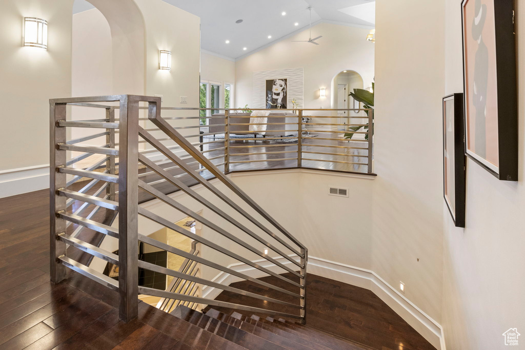 Staircase featuring arched walkways, wood-type flooring, baseboards, and lofted ceiling