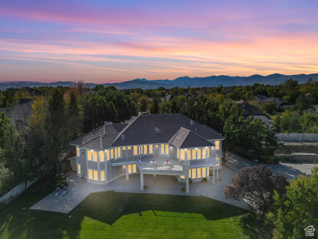 Back of house at dusk featuring a balcony, a patio, a mountain view, a tile roof, and stucco siding