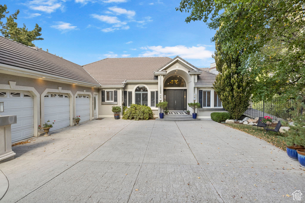 View of front of property featuring a tile roof, concrete driveway, an attached garage, and stucco siding