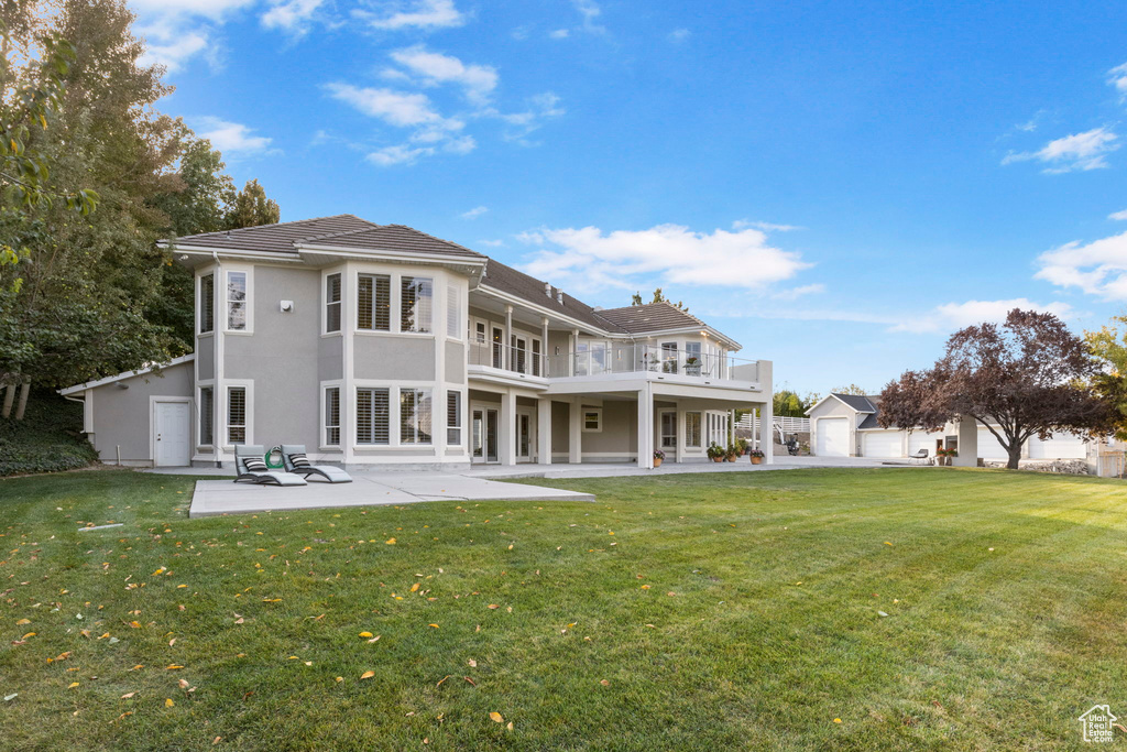 Back of property with a lawn, a balcony, a patio, and stucco siding