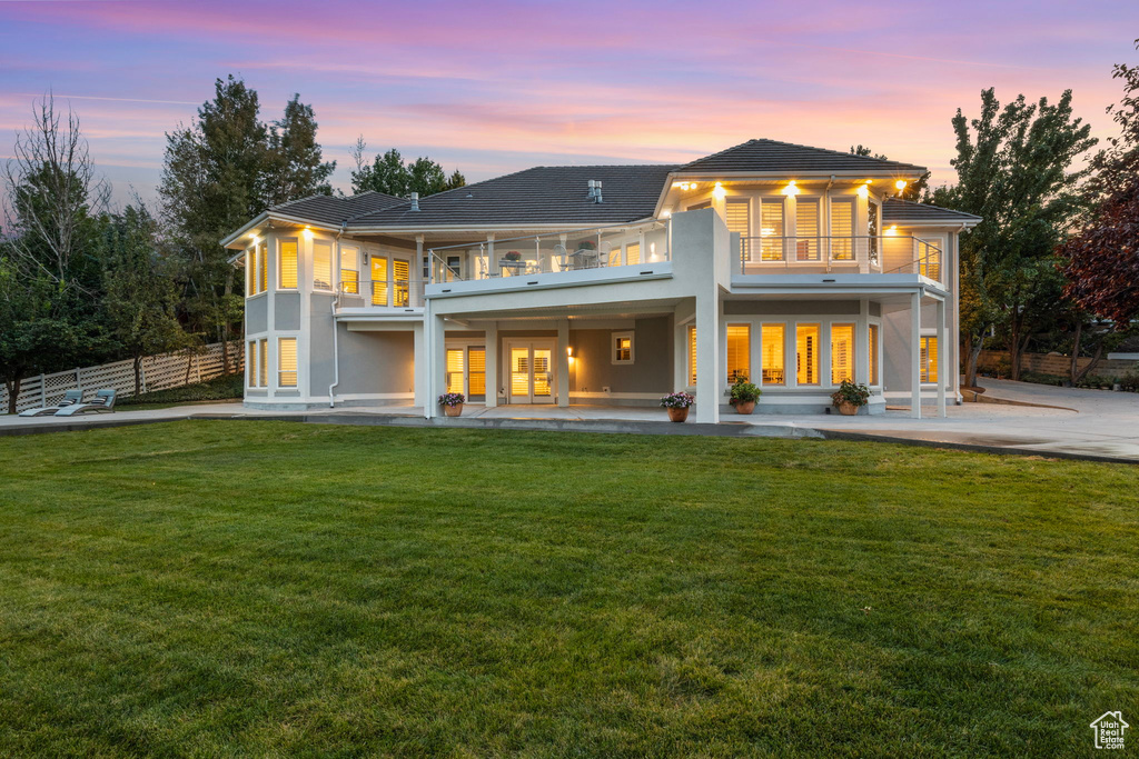 Back of property at dusk with a balcony, stucco siding, and a patio