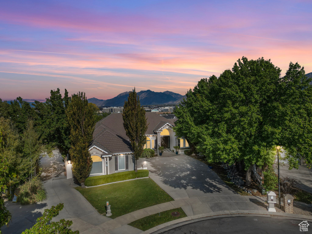View of front of house featuring a tiled roof, driveway, a mountain view, a lawn, and stucco siding